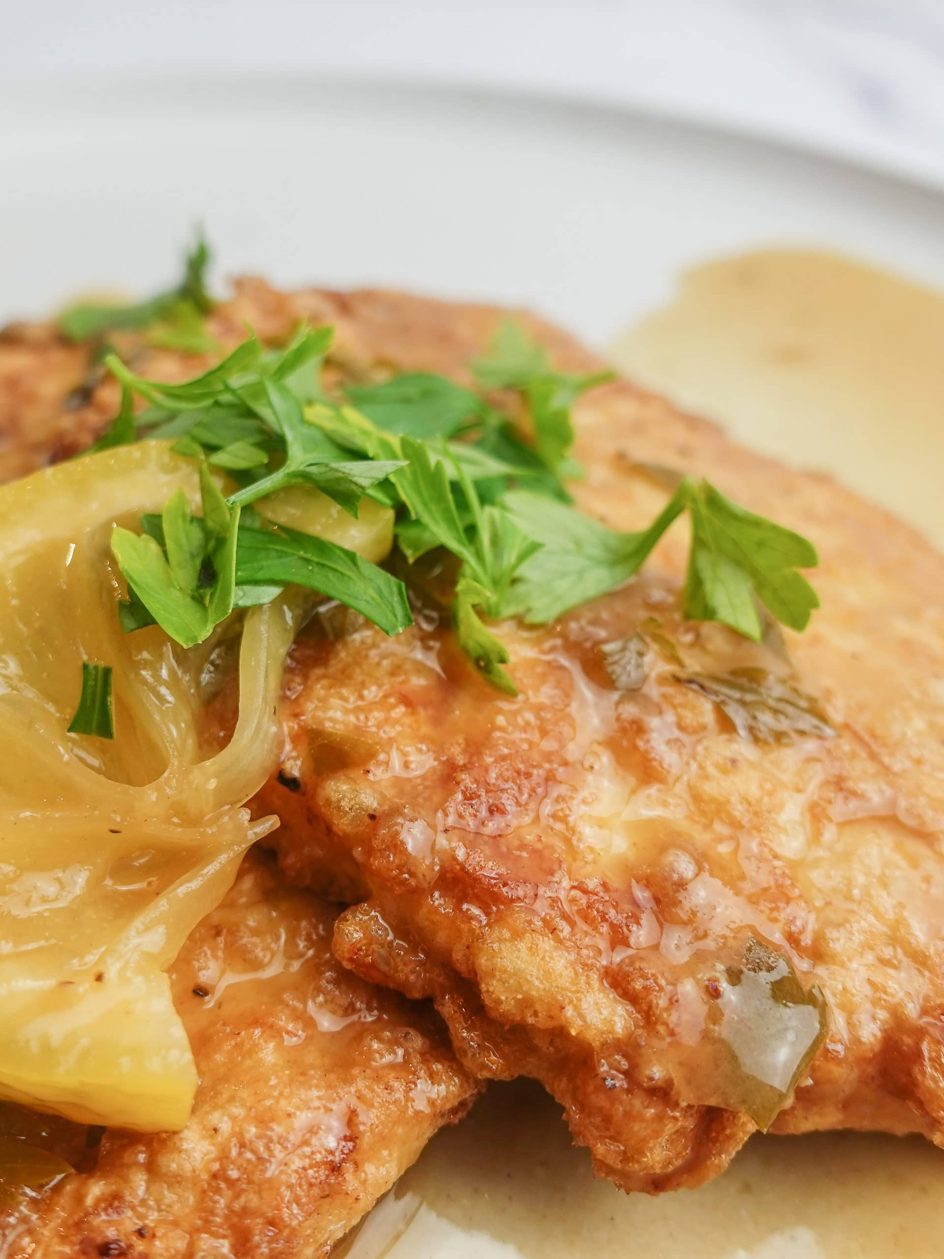 Chicken Francese on a white plate smothered in a thick Chicken Francese sauce with slices of lemon and garnished with chopped fresh Italian parsley.