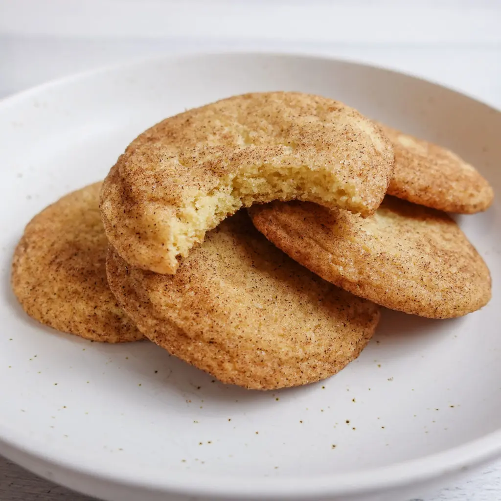 Delicious Snickerdoodle Cookies with a cinnamon sugar coating layered on top of a white ceramic plate.