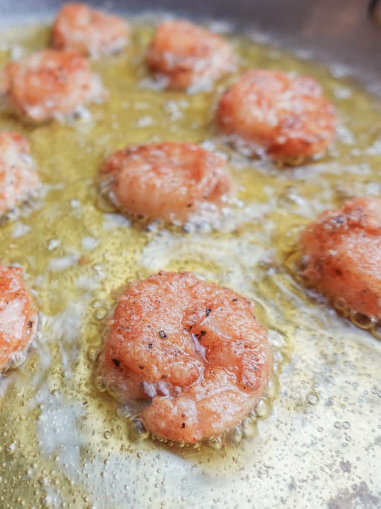 Closeup view of small shrimp frying in a pan of hot oil for crispy shrimp tacos.