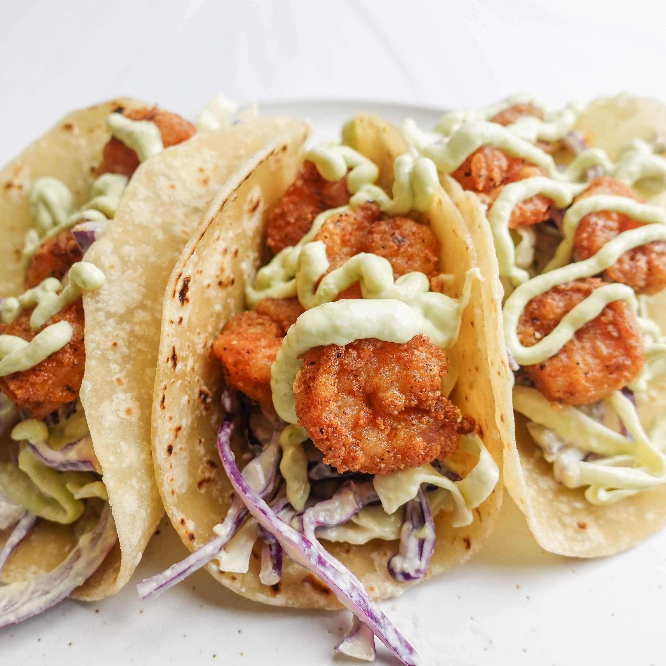 Front facing view of a crispy shrimp taco with an avocado lime slaw and avocado lime sauce drizzle on a homemade flour tortilla.