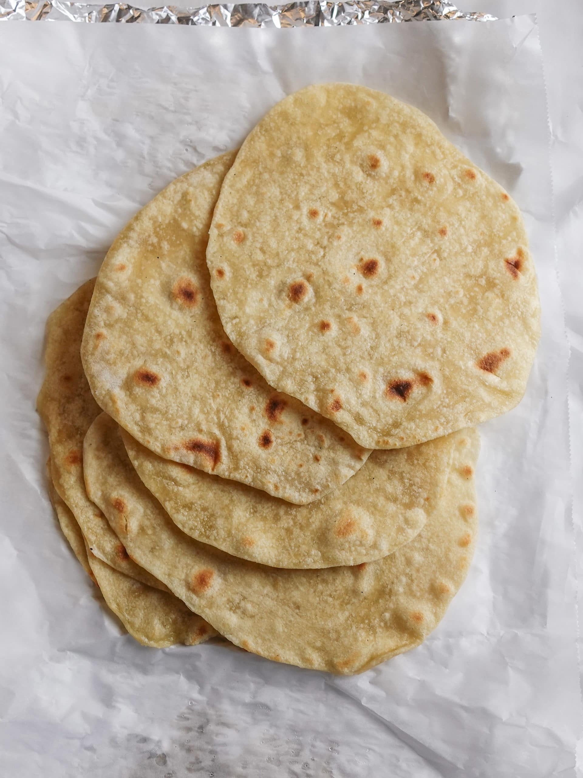 Overhead view of homemade flour tortillas stacked on top of one another on a sheet of parchment paper.