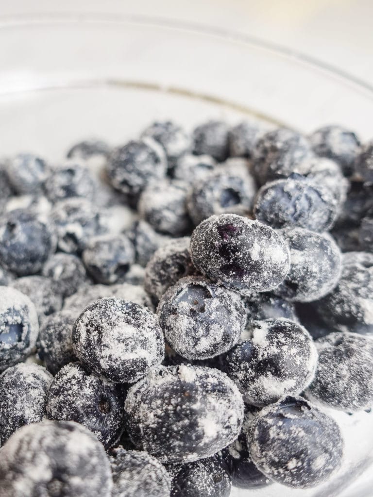 Blueberries coated in flour for lemon blueberry bread, in a transparent glass bowl.
