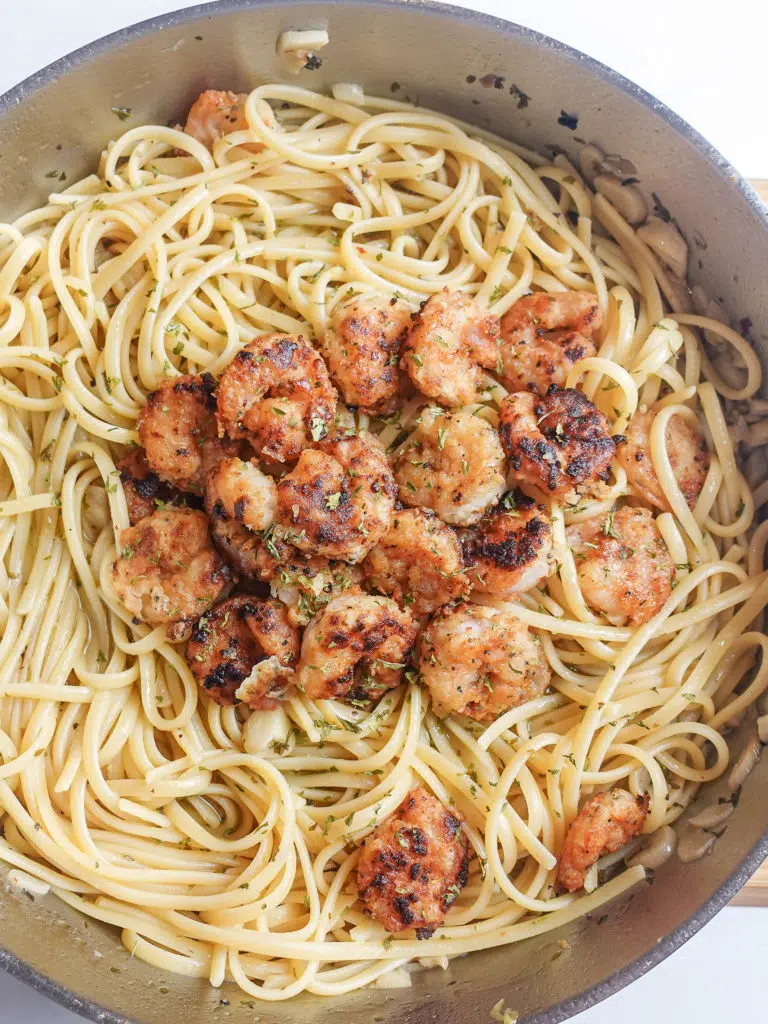 Overhead view of pan crusted shrimp over a bed of linguini in a butter, lemon, garlic, white wine sauce, garnished with a sprinkle of parsley.